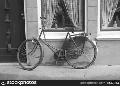 an old black bicycle parked on a wall with a window . an old black bicycle parked on a wall with a window