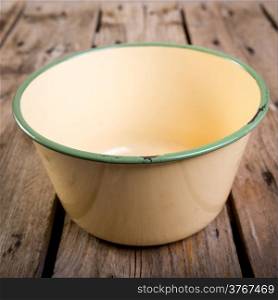 An old bowl in classic vintage colours with cracks and rust in shallow focus over a wooden table