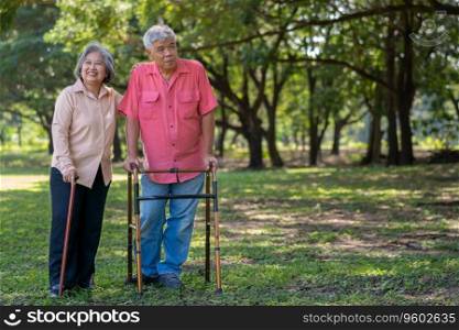 An old elderly Asian man uses a walker and walks in the park with his wife.  Concept of happy retirement With Love and care from family and caregiver, Savings, and senior health insurance