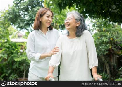 An old elderly Asian woman uses a walker and walking in the backyard with her daughter. Concept of happy retirement With care from a caregiver and Savings and senior health insurance