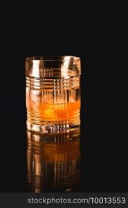 An Old Fashioned cocktail in a rocks glass that is sitting on the black reflective surface of an outdoor fire pit.