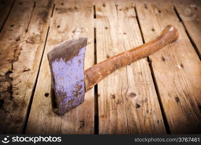 An old hatchet axe with a wooden handle and wear marks sits on a rough timber background