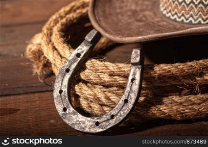 An old horseshoe lies next to a classic cowboy hat and lasso on a dark wooden background.. horseshoe hat lasso