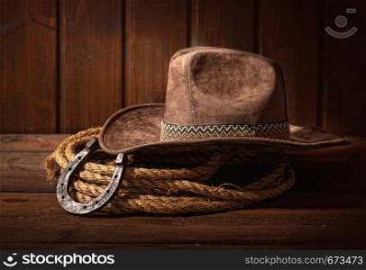 An old horseshoe lies next to a classic cowboy hat and lasso on a dark wooden background.. horseshoe hat lasso