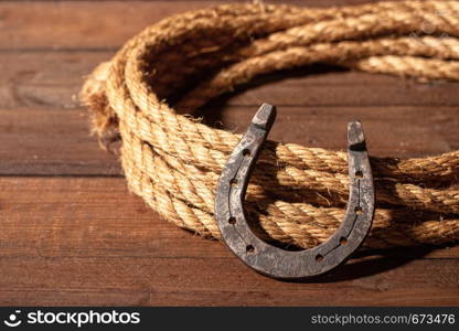 An old horseshoe lies next to a classic cowboy lasso on a dark wooden background.. horseshoe hat lasso