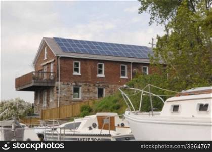 An old house outfitted with modern solar cells on the rooftop to harvestenergy from the sun, with sailboats in the foreground.