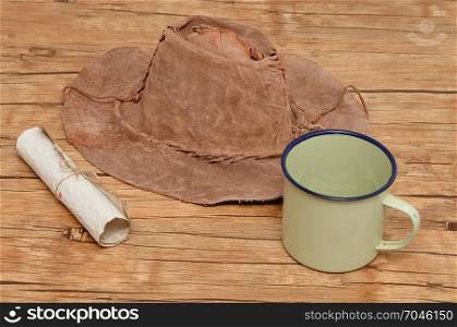 An old leather hat with a paper scroll and tin mug