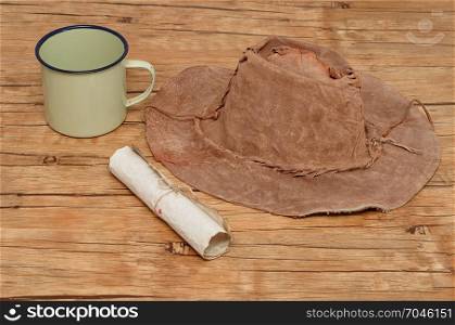 An old leather hat with a paper scroll and tin mug