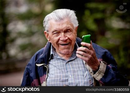 An old man laughing and smiling with a cell phone.