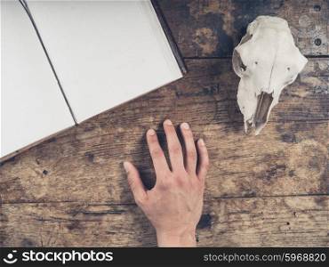 An old notebook with a sheep skull and the hand of a young man on a wooden desk