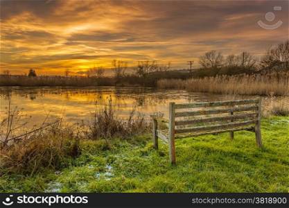 An old park bench looking across a frozen pond towards the setting sun