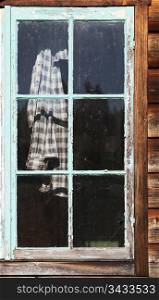 An old plaid work shirt hanging behind an old shed window with peeling and crackled turquoise paint.