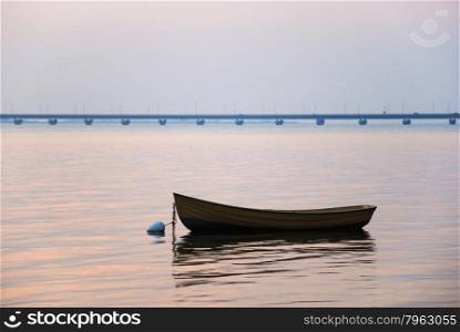 An old rowing boat anchored in a calm bay with the swedish Oland bridge in the background