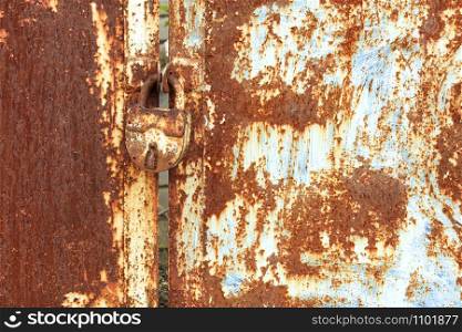 An old rusty door lock and an old metal sheet with rust texture and weathered aged peeling paint.. An old rusty lock connects a rusty gate. Rust on old metal sheet texture.