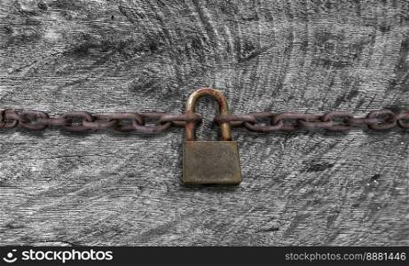 An old rusty padlock closed on a massive chain on vintage wooden table