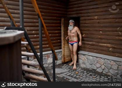 An old senior man at wooden outside sauna bathtub. Spa resort and thermal bath. An old senior man at wooden outside sauna bathtub