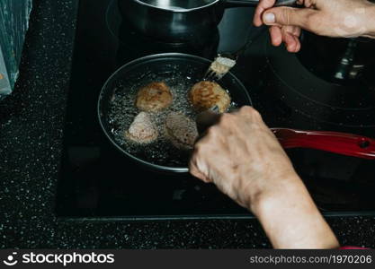 An old spanish woman frying meatballs on the kitchen