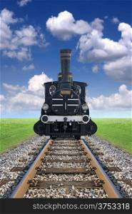 An old steam powered locomotive, railway track, green grass and blue sky on the horizon