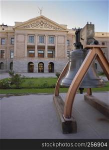 An old watchtower bell is mounted on the sidewalk in front of the state capitol building in Phoenix AZ