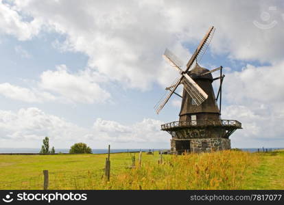 An old windmill is shown in a rural area. There are no people viewable. Horizontally framed shot.