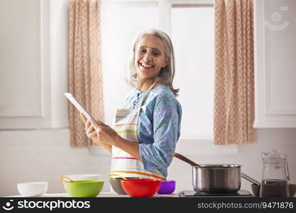 An old woman smiling in kitchen while holding a laptop with the recipe.