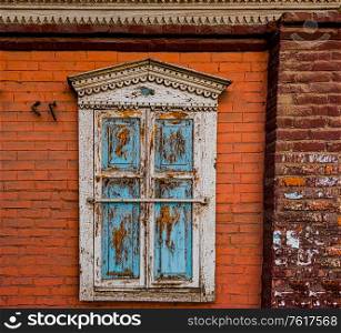 An old wooden carved window with shutters closed on the wall of a brick house