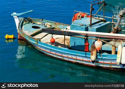 An old wooden fishing boat with raised oars and bright plastic buoys is anchored against the blue water of the Ionian Sea, image with copy space.. An old fishing boat anchored in the clear waters of the Ionian Sea.