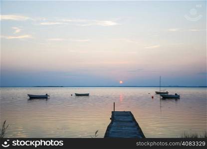 An old wooden jetty with anchored small boats in a calm bay at twilight time