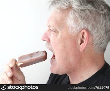 An older man eats a chocolate-covered ice cream bar.