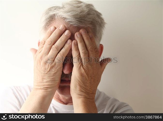 An older man hides his face in embarrassment or grief.