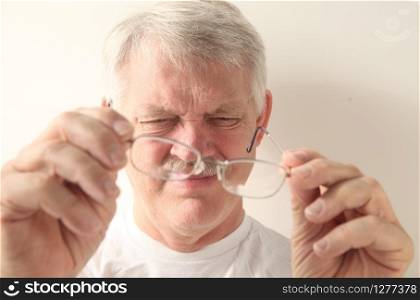 An older man squints at his glasses.