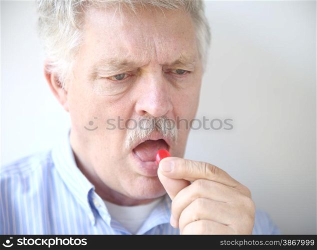 An older man takes a throat lozenge for a sore throat.