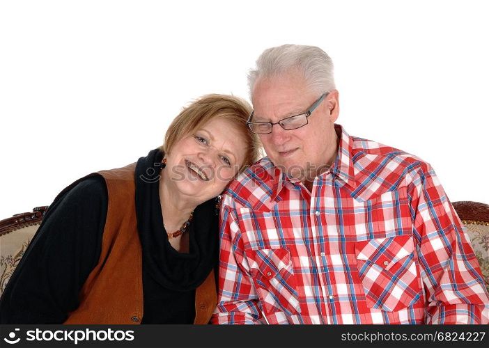 An older senior citizen couple sitting on a sofa, the wife with her headon the shoulder of her husband, isolated for white background.
