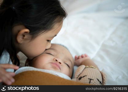 An older sister hugs her newborn little sister while she sleeps. In the white bedroom, warm sunlight in the evening of the day.