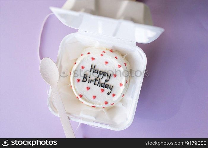 An open box with a bento cake and a wooden spoon for a birthday on a purple background. An open box with a birthday bento cake on a purple background