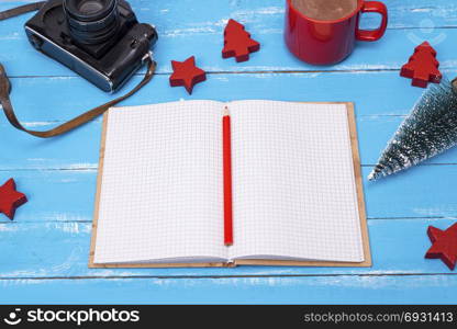 an open empty school notebook, an old film camera and a cup of hot cocoa on a blue wooden background