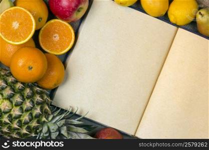 An open menu book with blank pages and a selection of fresh fruit.