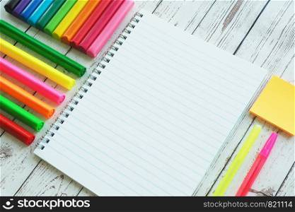 An open notebook, colorful bright markers, pens and clay on a wooden background.
