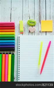 An open notebook, colorful bright markers, pens, sharpener, eraser, stickers and clay on a wooden background.