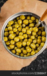 An open tin can with canned green peas on paper. On a black background. High quality photo. An open tin can with canned green peas on paper.