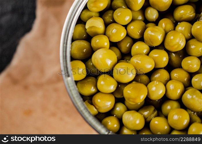 An open tin can with canned green peas on paper. On a black background. High quality photo. An open tin can with canned green peas on paper. 