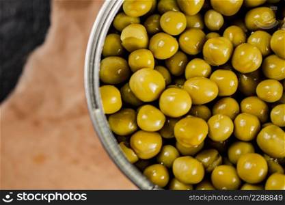 An open tin can with canned green peas on paper. On a black background. High quality photo. An open tin can with canned green peas on paper. 