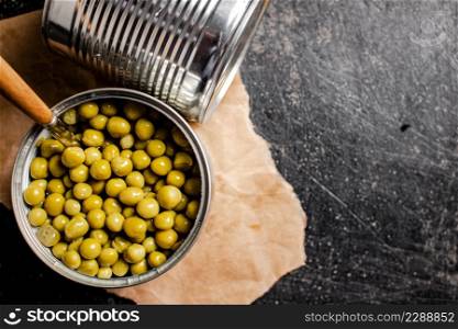 An open tin can with canned green peas on paper. On a black background. High quality photo. An open tin can with canned green peas on paper.