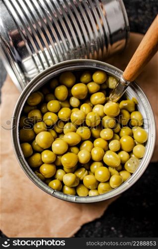 An open tin can with canned green peas on paper. On a black background. High quality photo. An open tin can with canned green peas on paper.