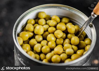 An open tin can with green peas. On a black background. High quality photo. An open tin can with green peas. 