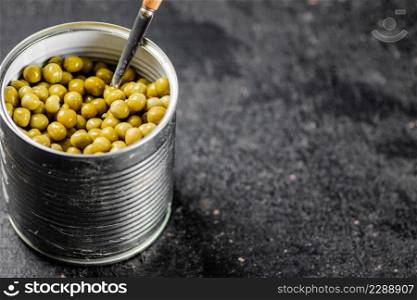 An open tin can with green peas. On a black background. High quality photo. An open tin can with green peas.