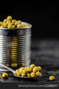 An open tin can with green peas. On a black background. High quality photo. An open tin can with green peas.