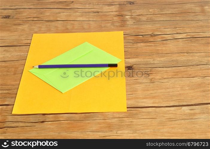 An orange paper and a green envelope with a writing pencil