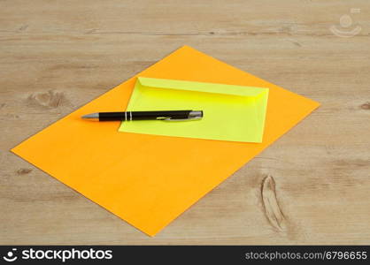 An orange paper and a yellow envelope with a black pen