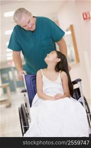 An Orderly Pushing A Little Girl In A Wheelchair Down A Hospital Corridor